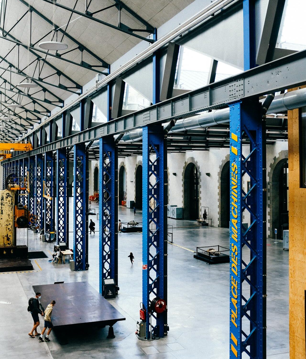 Interior view of a large industrial space with blue steel beams and machinery at Place des Machines.