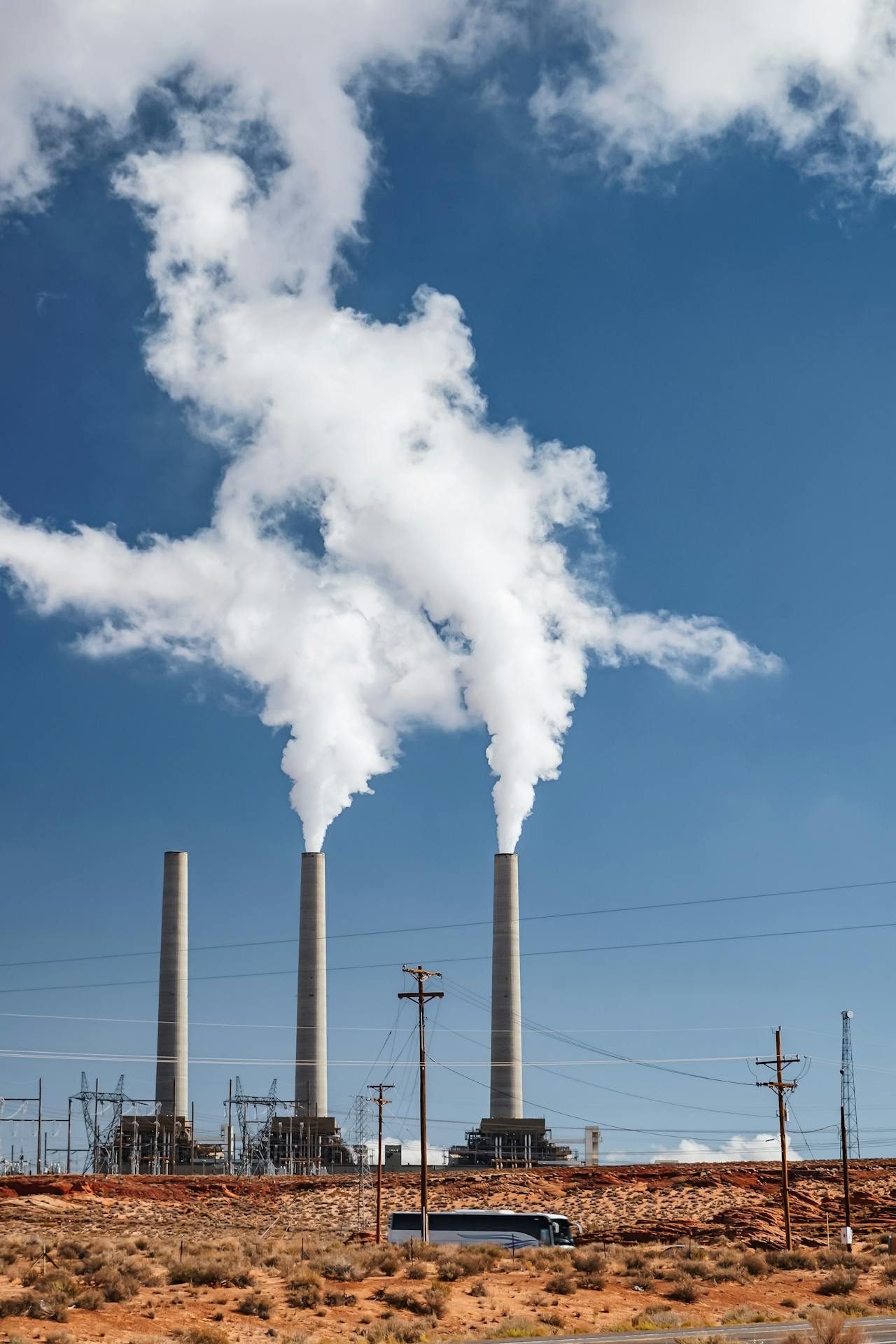 Three smokestacks emitting white steam against a blue sky with scattered clouds.