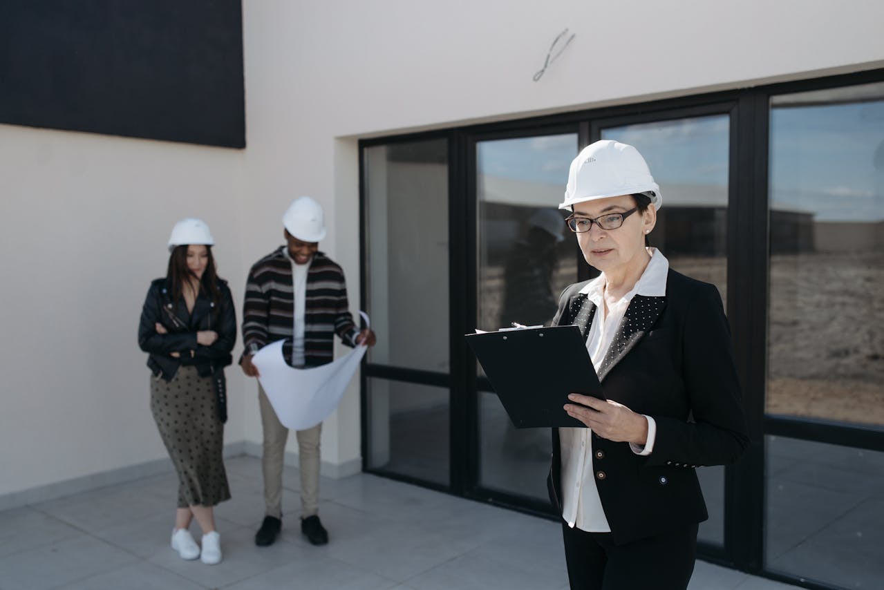 Pavel Danilyuk photograph features a woman in a black blazer and white hard hat holding a clipboard, accompanied by two colleagues in safety gear outside a modern building.