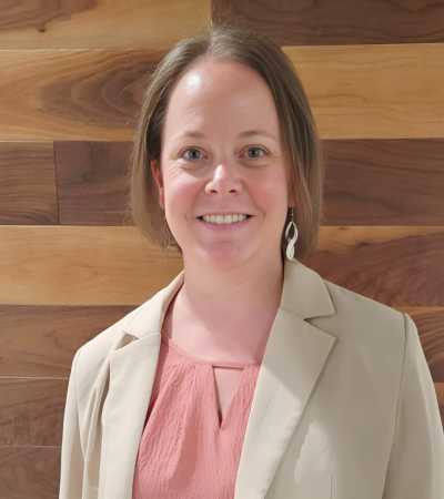 Katie Gjerde posing in a beige blazer against a wooden backdrop.