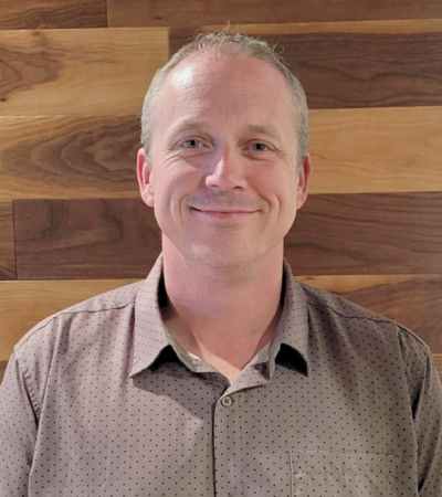 Ole Gjerde smiling in a button-up shirt against a wooden background.