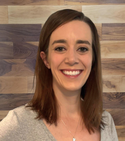 Woman with shoulder-length brown hair smiling against a wooden background.